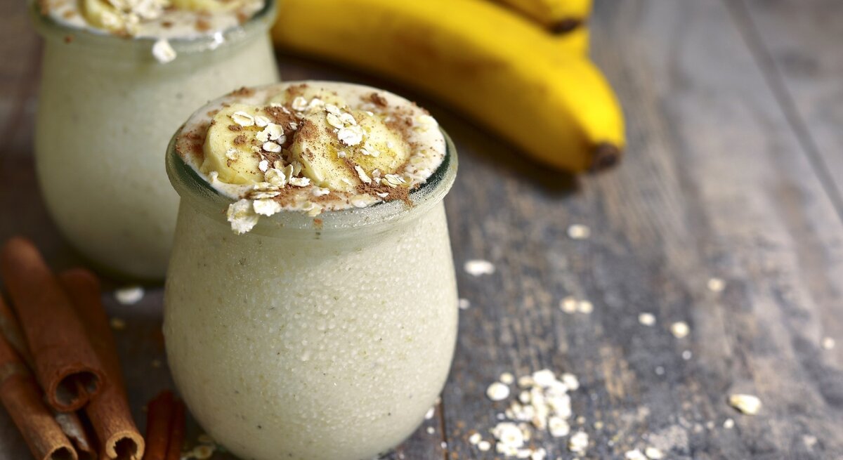 Bananenpudding im Glas – dekoriert mit Haferflocken und Banane auf hölzernem Untergrund.