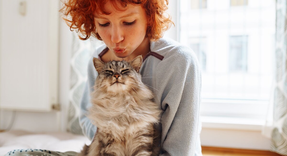 Rothaarige Frau gibt Katze einen Kuss